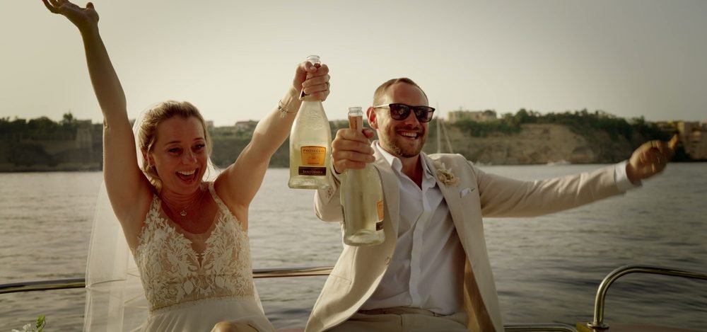 Gli sposi con lo champagne in barca nella luce dorata